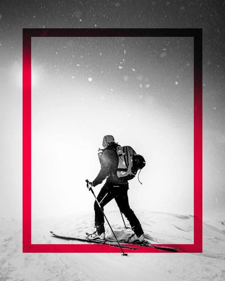 Ski tourer climbing through a snowstorm, framed by a pink border